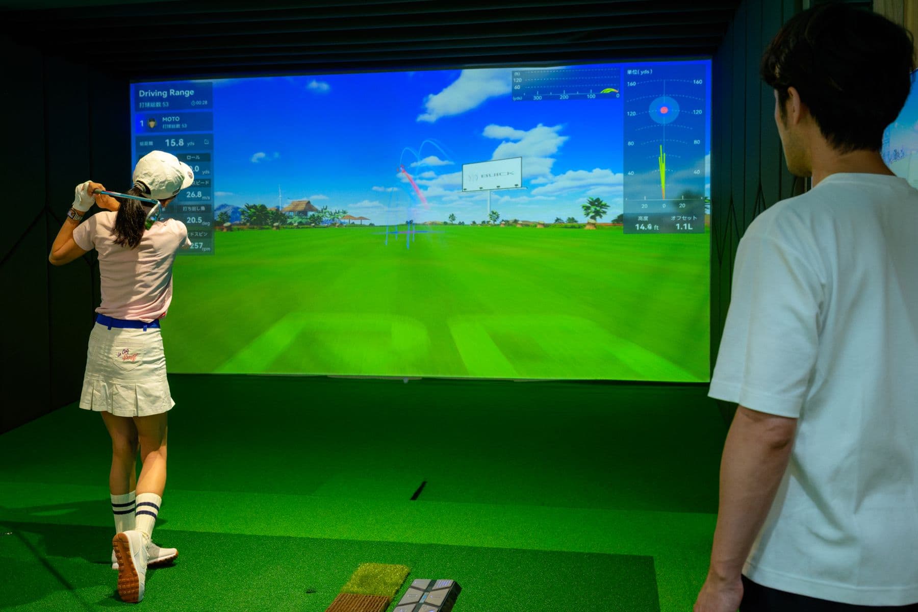 Student swinging at the simulator while the coach watches
